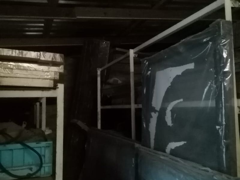 A cluttered utility or storage space featuring metal shelving units and exposed timber ceiling joists.
