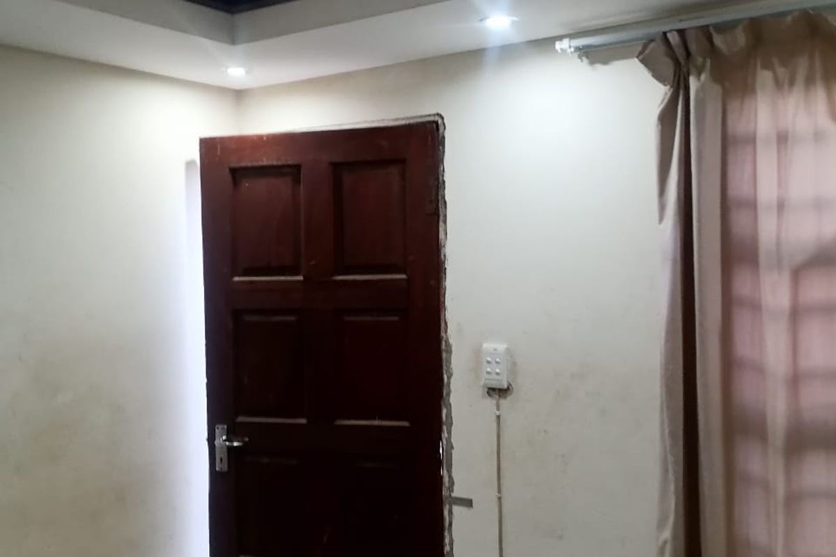 A bedroom featuring recessed ceiling lighting, tiled floors, and a timber door, currently showing signs of wall damage and exposed electrical conduit.