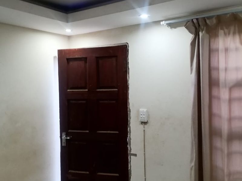 A bedroom featuring recessed ceiling lighting, tiled floors, and a timber door, currently showing signs of wall damage and exposed electrical conduit.