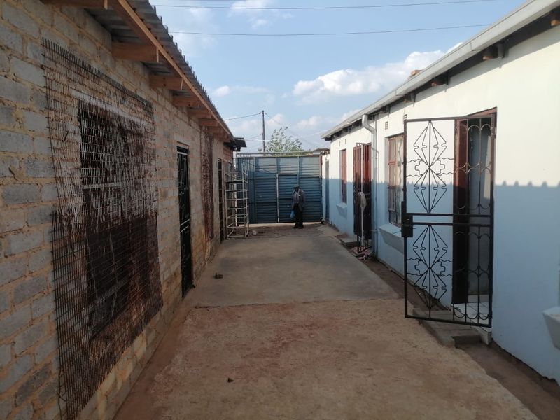 Exterior view of a residential property featuring a concrete pathway between two structures with security gates and unfinished brickwork.