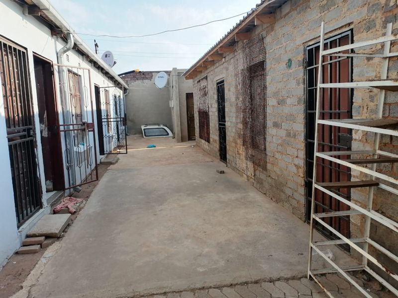A narrow exterior rear courtyard area featuring concrete paving, exposed brick walls, and multiple security-gated entrances to the apartment units.