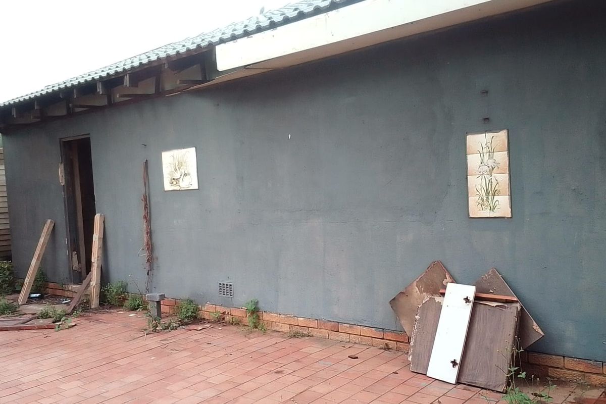 Rear exterior view of the property featuring a paved patio area and plastered wall with visible maintenance requirements.