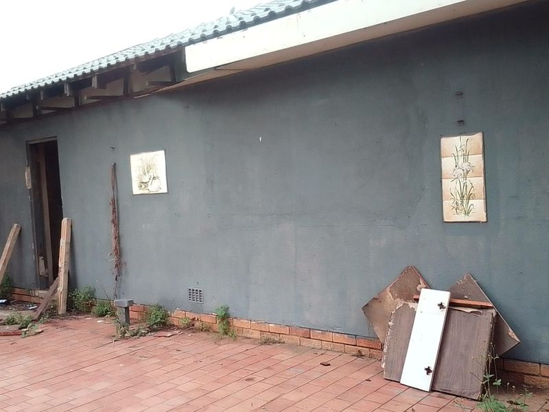 Rear exterior view of the property featuring a paved patio area and plastered wall with visible maintenance requirements.