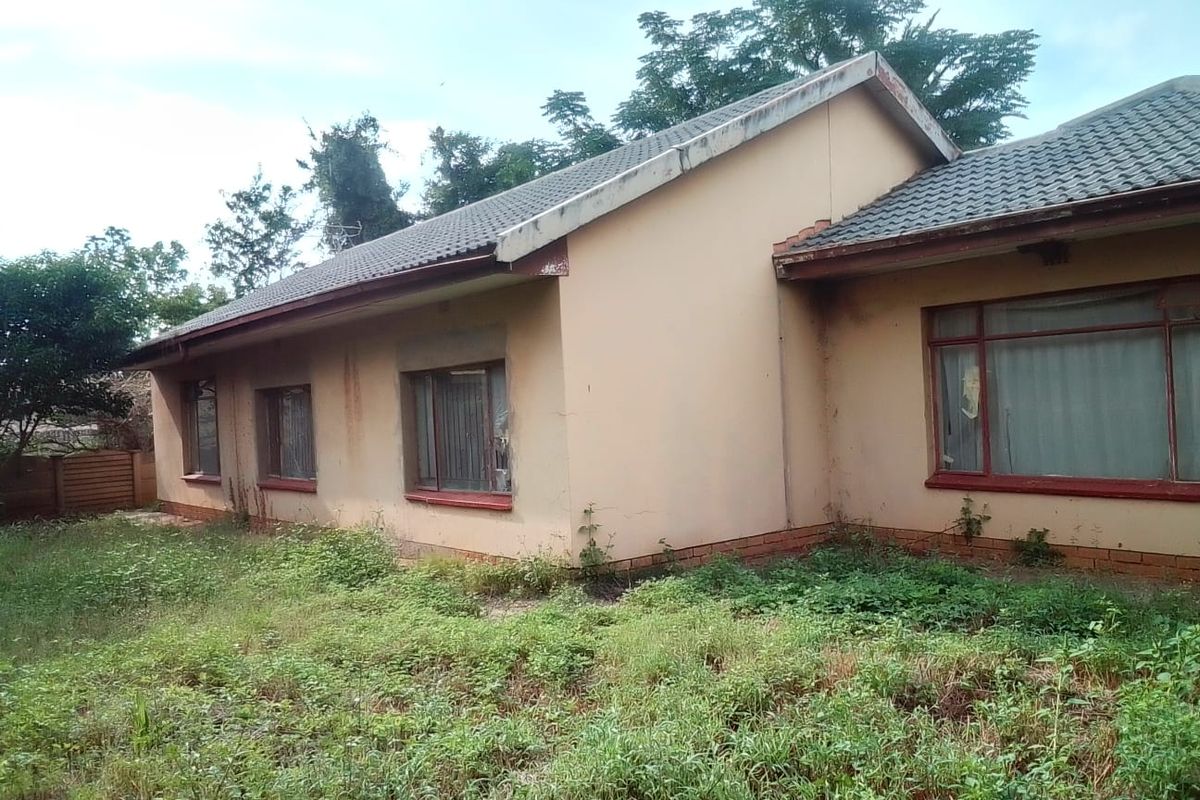 Rear exterior view of a single-story house featuring a tiled roof and brick facade, currently requiring significant maintenance and landscaping.