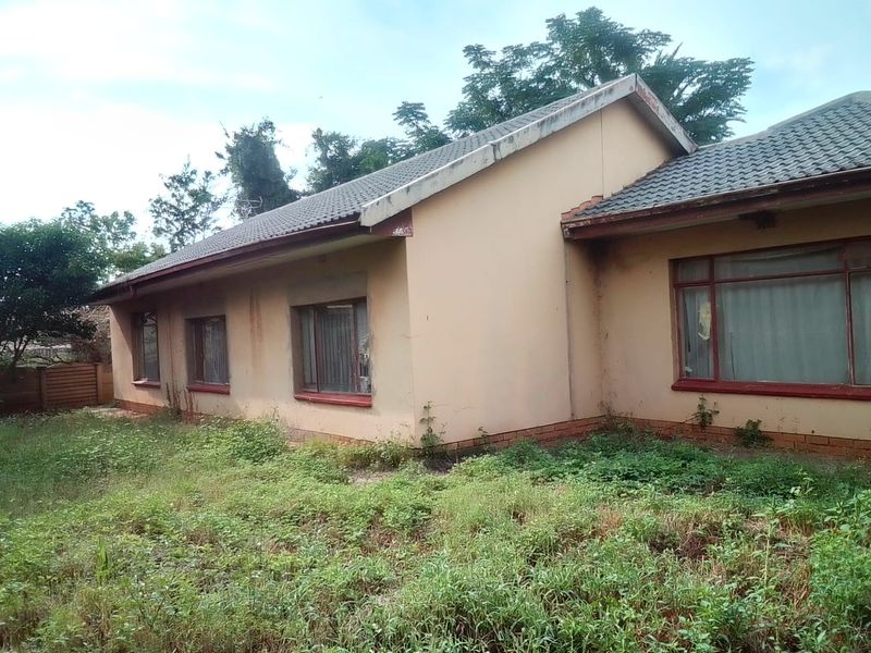 Rear exterior view of a single-story house featuring a tiled roof and brick facade, currently requiring significant maintenance and landscaping.