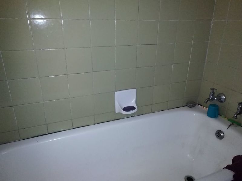 A dated bathroom featuring a standard bathtub with wall-mounted fixtures and olive-toned ceramic wall tiling.