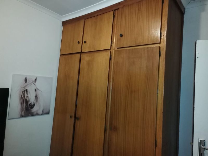 A bedroom featuring floor-to-ceiling wooden built-in cupboards providing ample storage space.