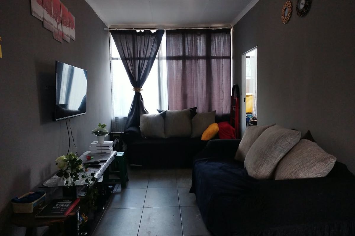 A living room featuring tiled flooring and a large window, providing natural light to the space.
