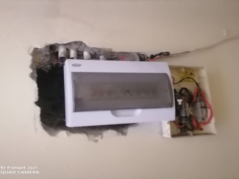 An electrical distribution board installed on a wall with incomplete plastering and exposed wiring, requiring professional repair and finishing.