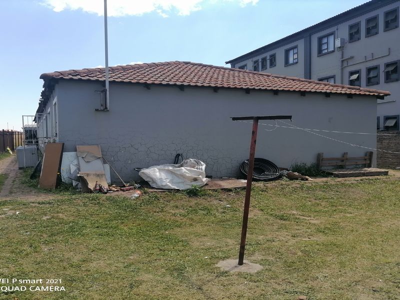 Rear view of the property showing a tiled roof, exterior wall with visible plaster cracking, and a metal washing line in the backyard area.