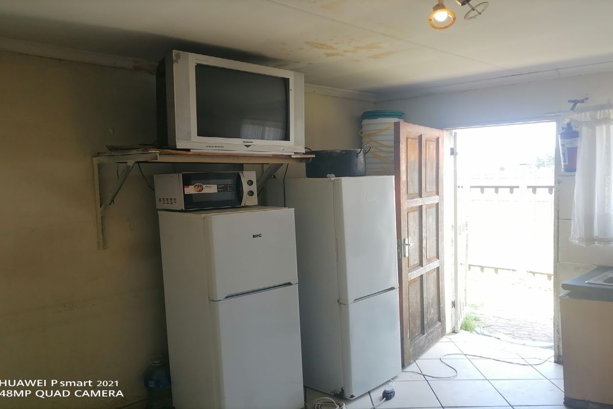 A dated kitchen area featuring tiled floors, basic cabinetry, and a sink, requiring cosmetic updates and ceiling repairs.