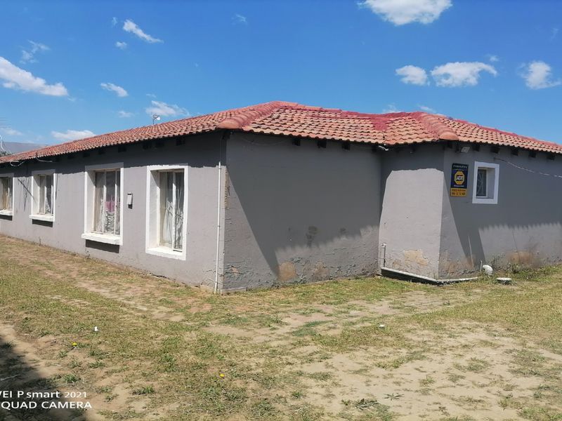 Rear exterior view of a single-story house featuring a terracotta tiled roof and painted masonry walls with visible signs of wear.