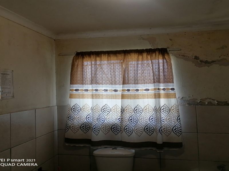 A bathroom featuring tiled walls and a toilet, currently showing significant signs of wall surface deterioration and peeling paint requiring maintenance.