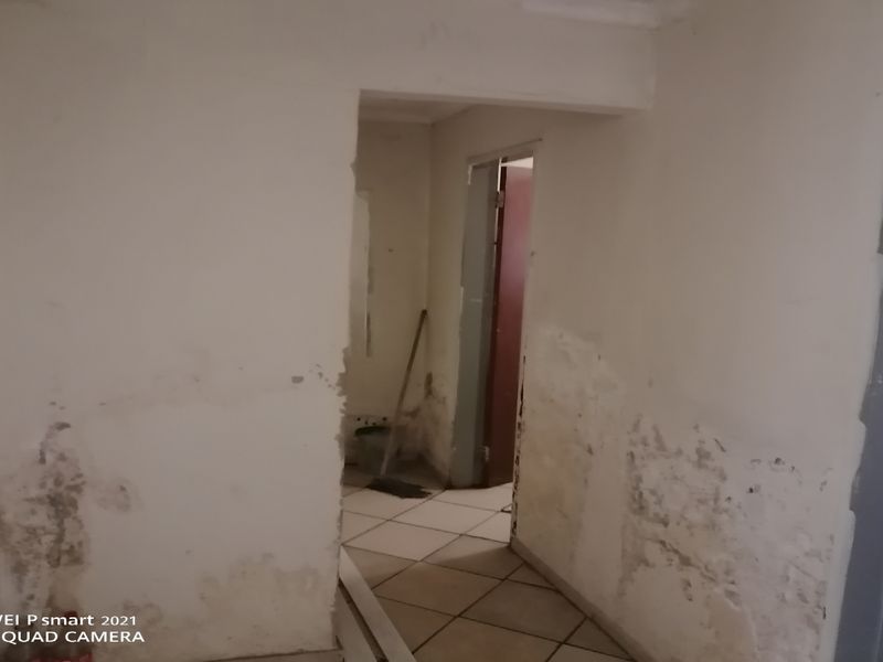 A vacant hallway featuring tiled flooring and walls requiring significant repair and repainting due to visible surface damage and signs of damp.