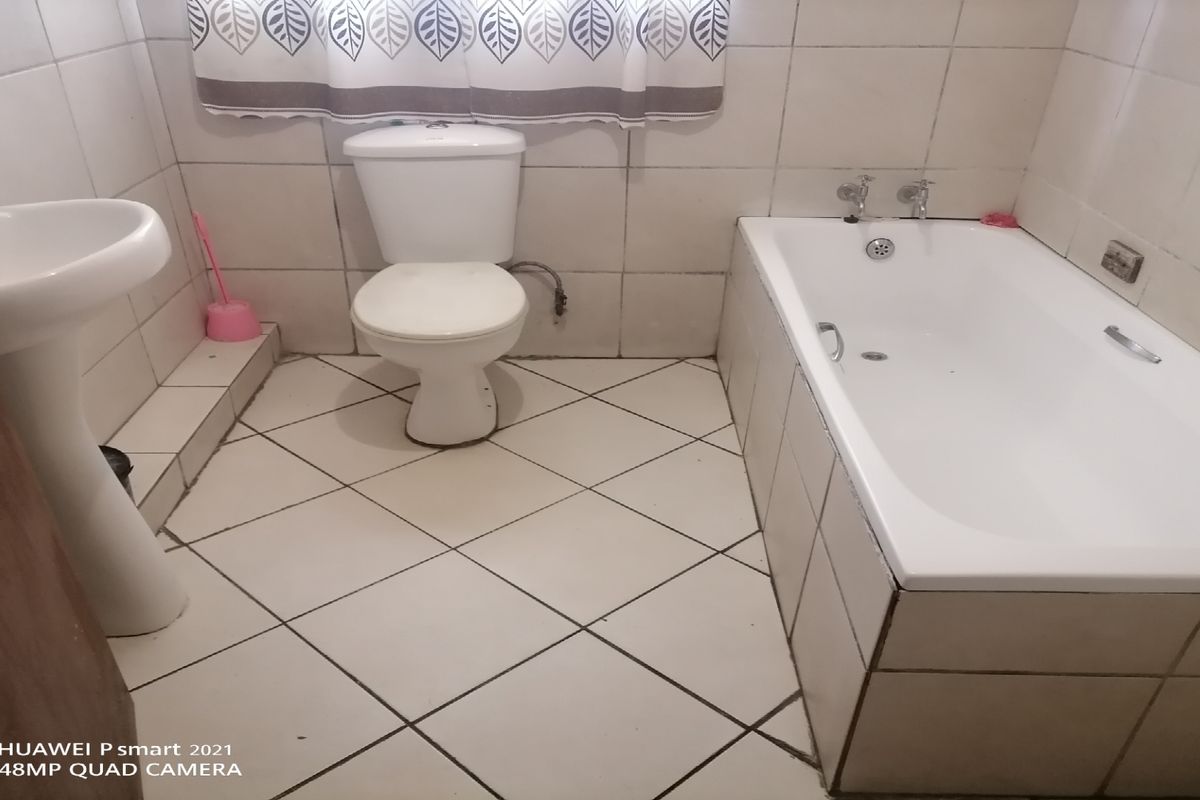 A functional bathroom featuring a pedestal basin, standard toilet, and a built-in bathtub with full-height wall tiling.