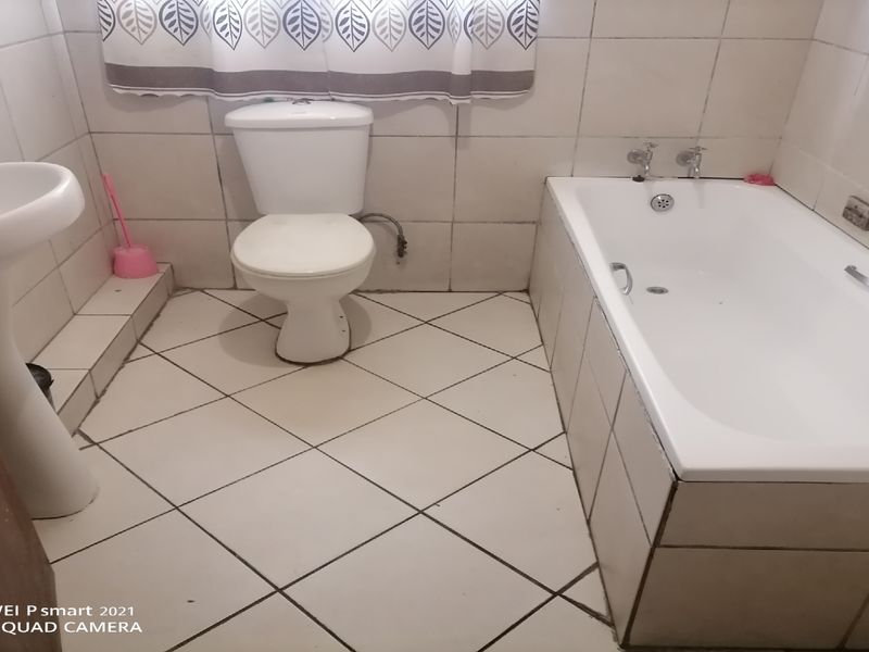 A functional bathroom featuring a pedestal basin, standard toilet, and a built-in bathtub with full-height wall tiling.