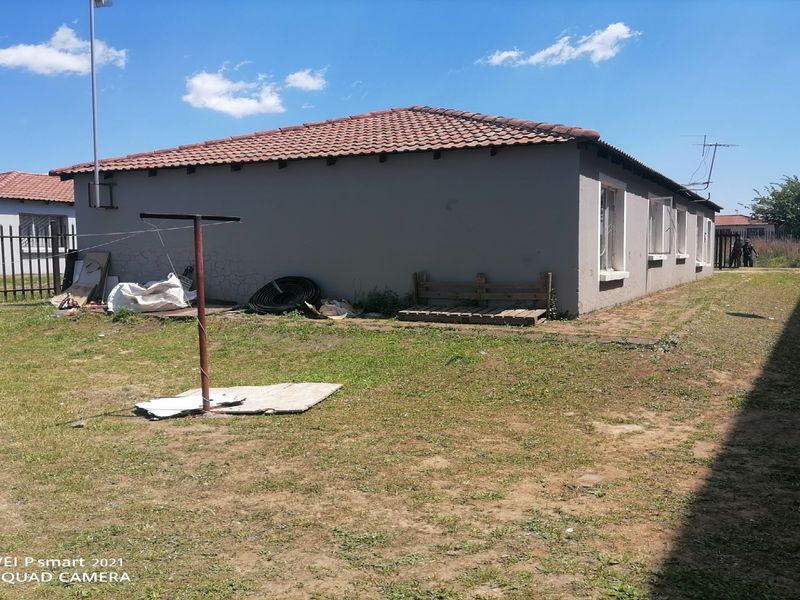 A view of the rear exterior of the house featuring a tiled roof, metal perimeter fencing, and a large, unlandscaped yard area.