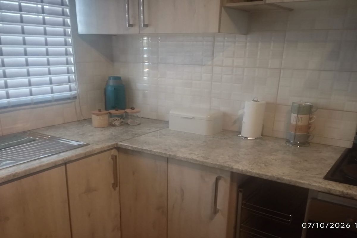 A functional kitchen featuring light wood-look cabinetry, stone-effect countertops, a tiled backsplash, and a stainless steel sink with integrated hob.