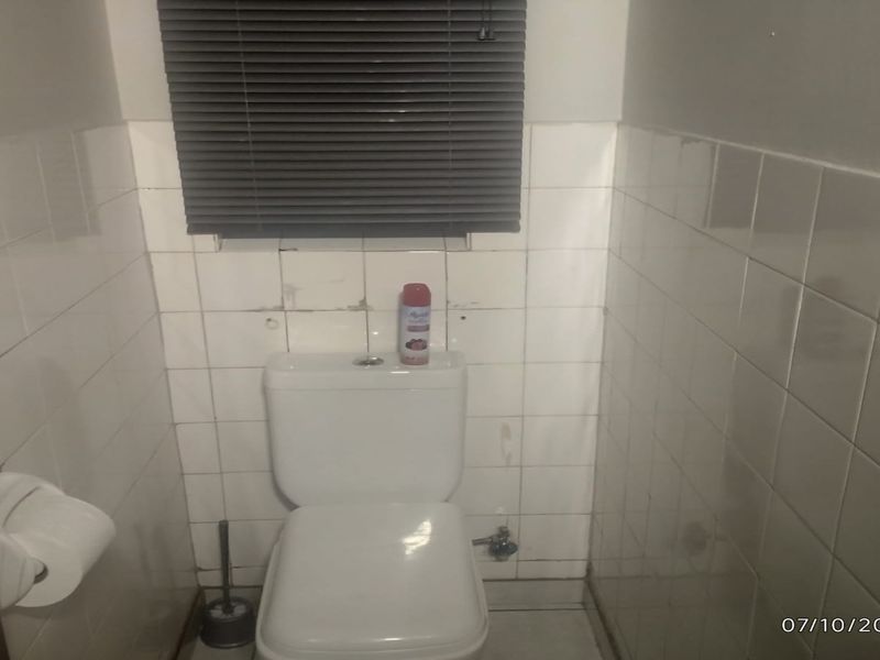 A compact bathroom featuring a standard toilet, tiled walls, and a window blind. The space requires cosmetic updates to the tiling and wall finishes.