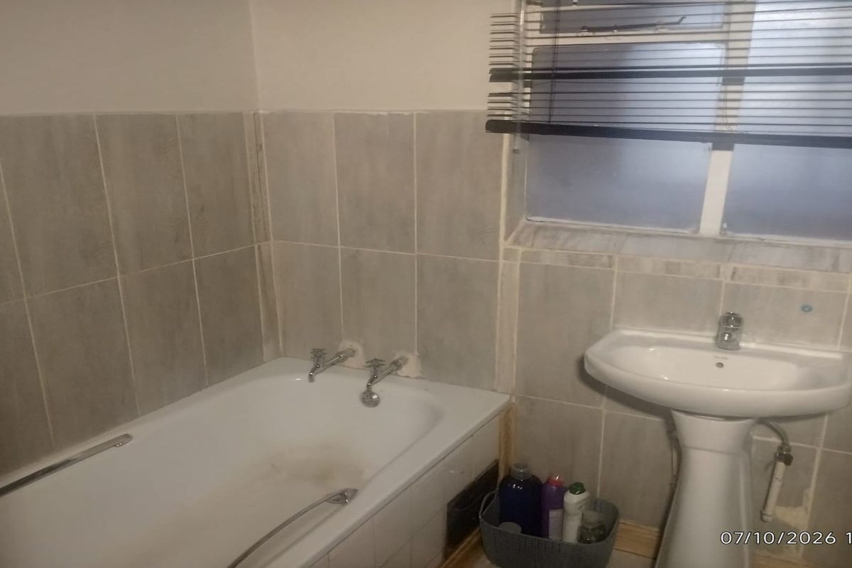 A functional bathroom featuring a bathtub, pedestal basin, and wall tiling, currently requiring cosmetic updates and maintenance to improve its overall condition.