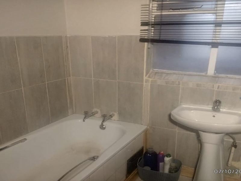 A functional bathroom featuring a bathtub, pedestal basin, and wall tiling, currently requiring cosmetic updates and maintenance to improve its overall condition.