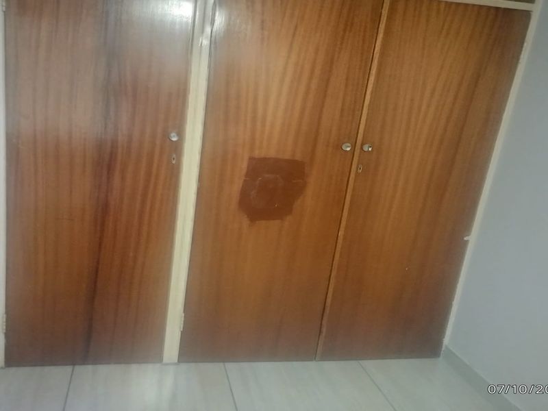 A bedroom featuring built-in wooden cupboards with visible surface damage and tiled flooring.
