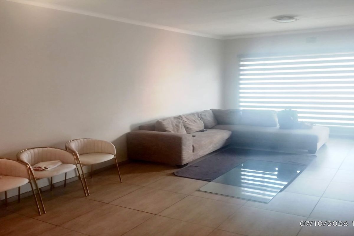 A spacious living room featuring neutral tiled flooring, coved ceilings, and large windows fitted with modern roller blinds.