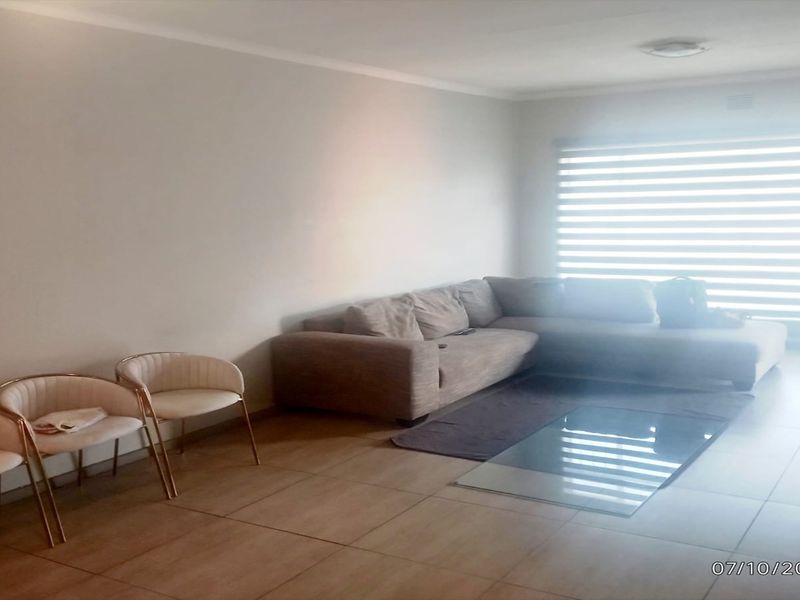A spacious living room featuring neutral tiled flooring, coved ceilings, and large windows fitted with modern roller blinds.