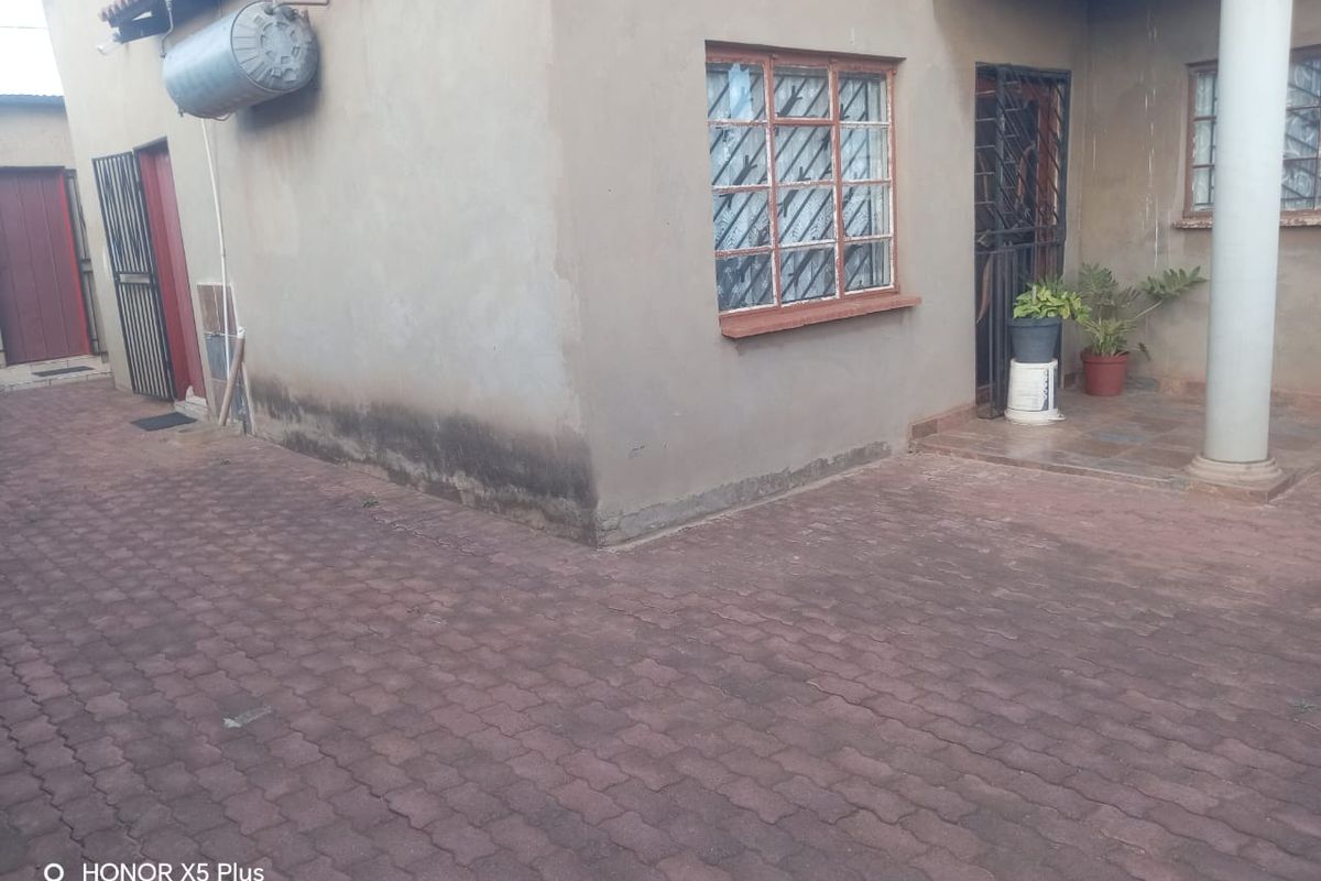 Rear exterior view of the property featuring paved ground, security gates, window bars, and an external geyser unit.