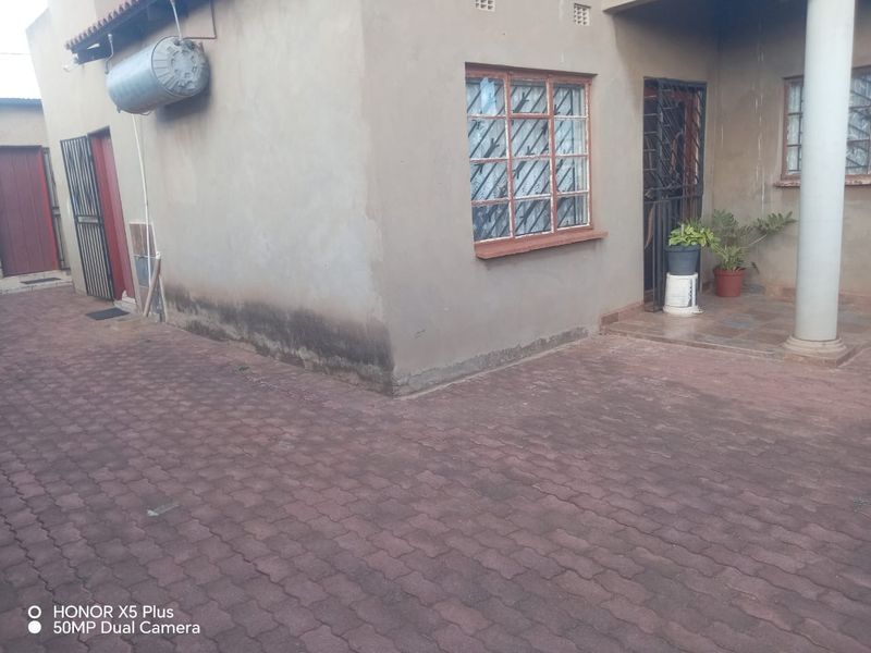 Rear exterior view of the property featuring paved ground, security gates, window bars, and an external geyser unit.