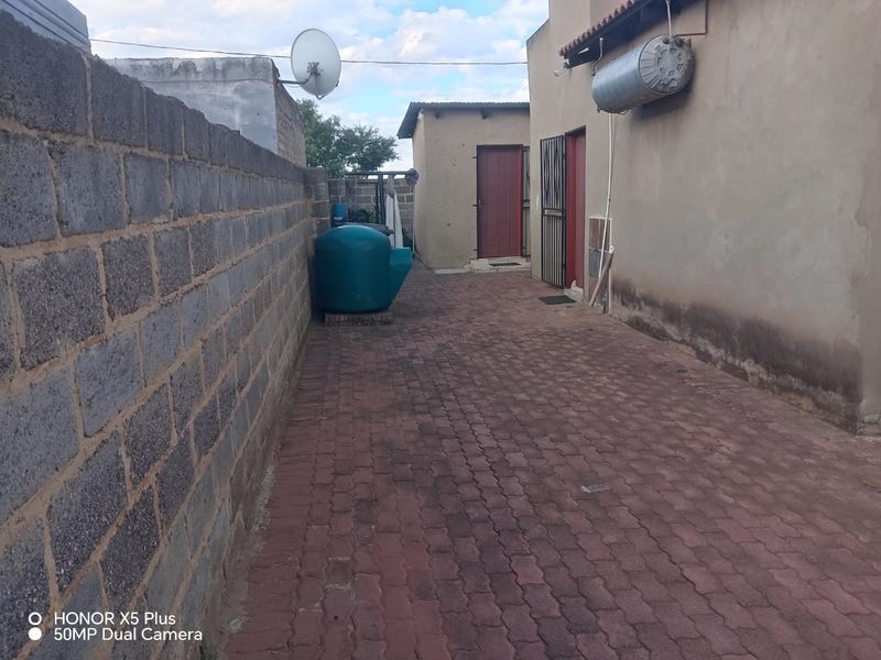 Rear exterior area featuring paved ground, a cinder block boundary wall, and a wall-mounted solar water heater.