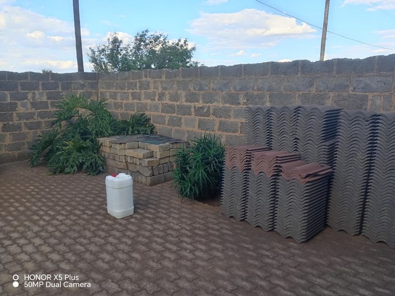 A rear outdoor area featuring a concrete block boundary wall and paved ground, currently used for storage of construction materials.