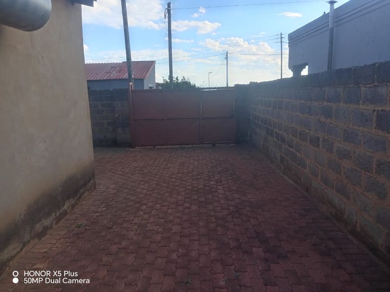 A paved driveway area enclosed by a perimeter wall and metal gate, showing signs of exterior wear.