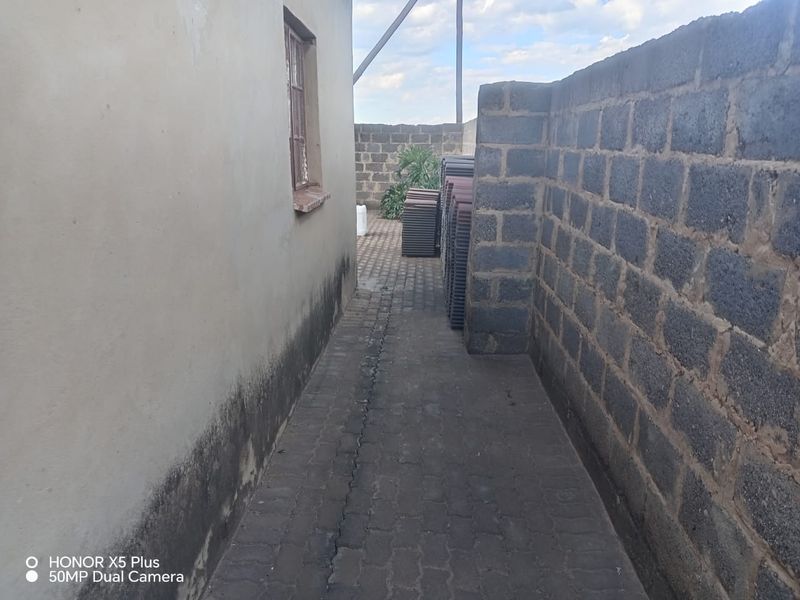 A narrow side passage featuring paved flooring, a concrete block boundary wall, and visible signs of damp on the exterior building wall.