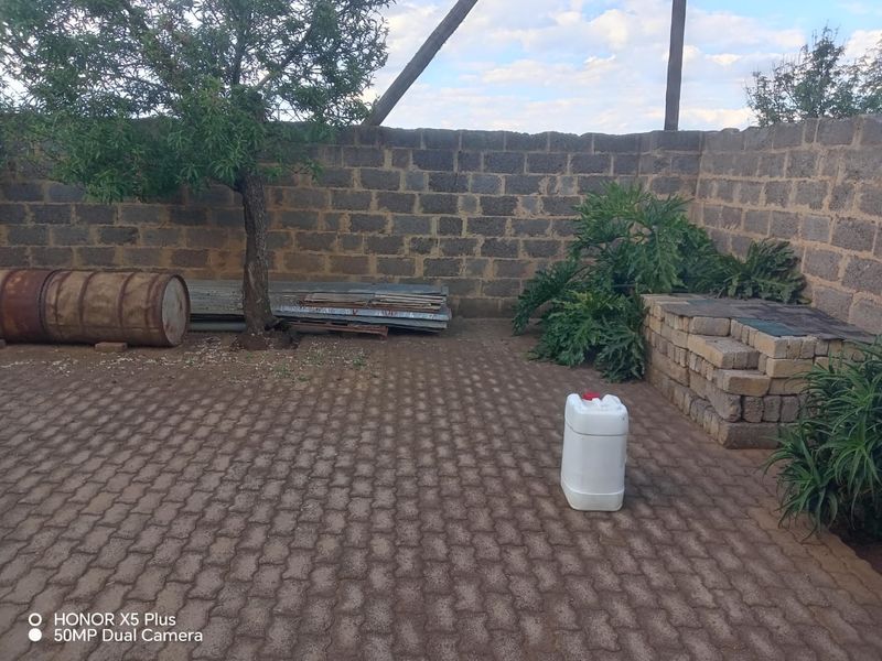 A paved rear outdoor area featuring a cinder block boundary wall and brick retaining structure, currently requiring maintenance and clearing.