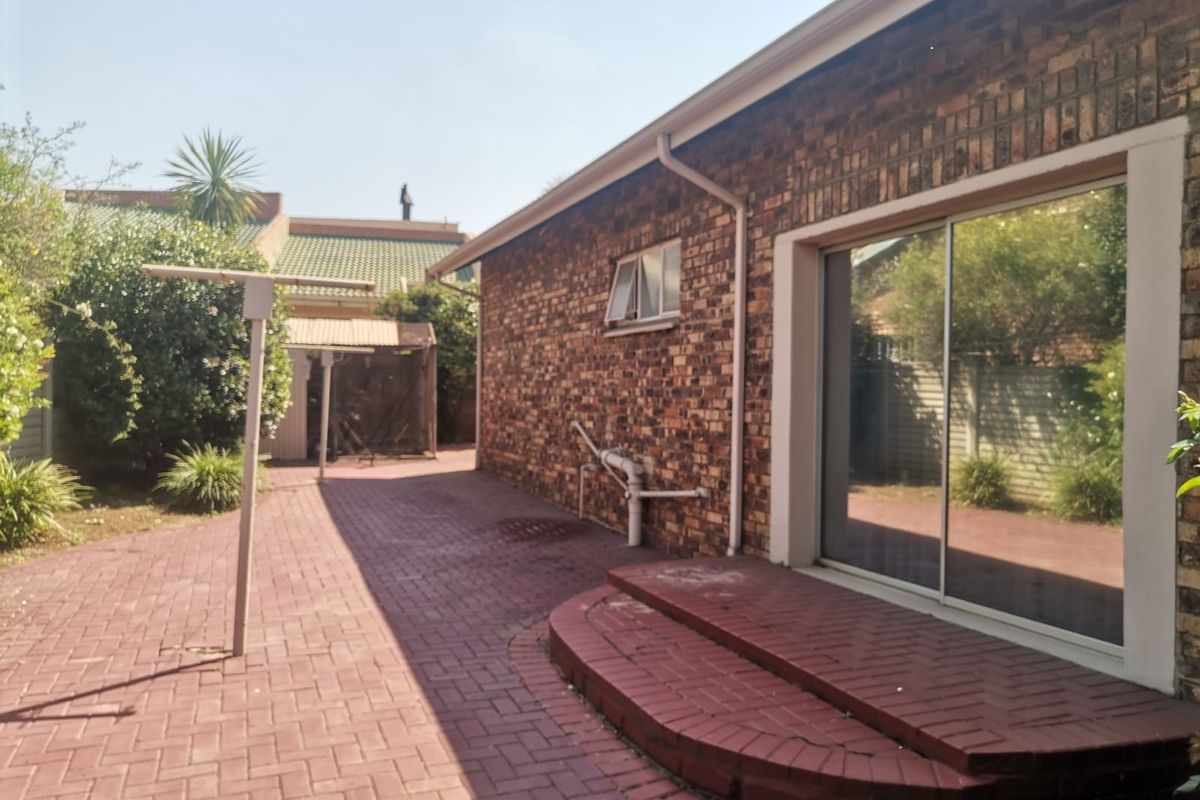 Rear exterior view of the property featuring a brick facade, paved patio area, and sliding glass door access.