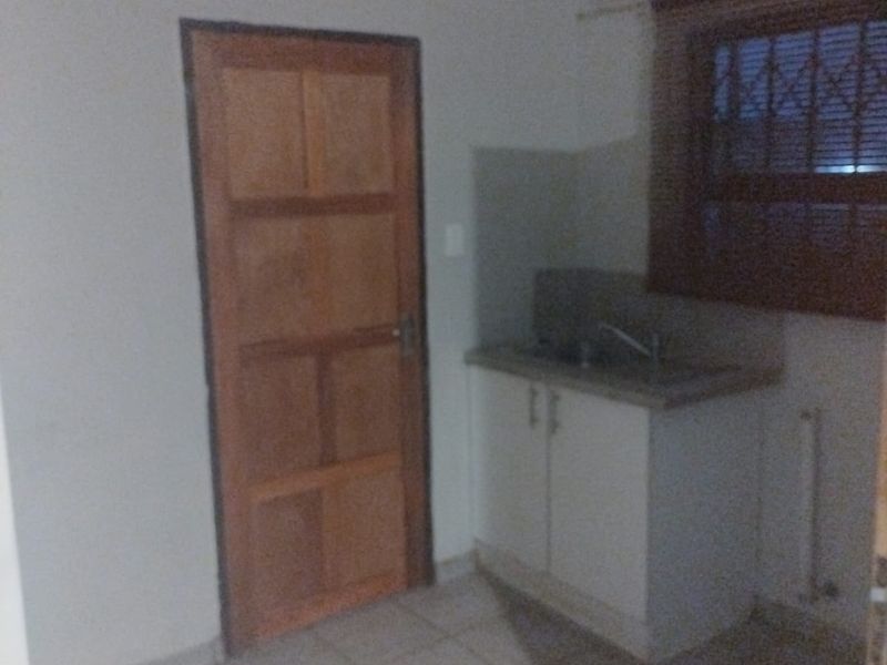 A small, functional scullery or utility area featuring tiled flooring, a built-in sink with base cabinetry, and a window with security bars.