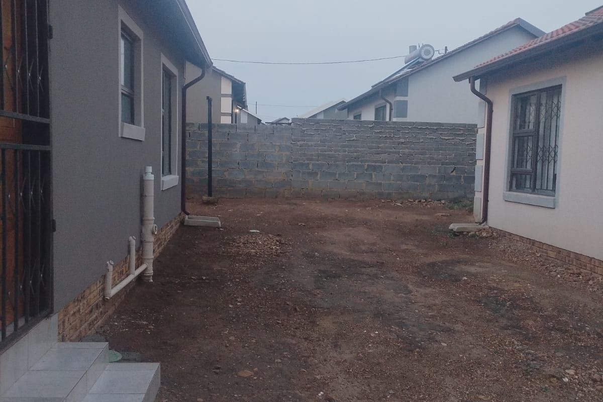 Rear exterior view showing a side passage between two structures with tiled steps, security bars, and an unlandscaped dirt yard area.