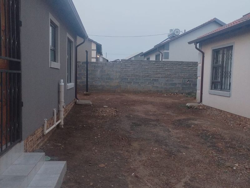 Rear exterior view showing a side passage between two structures with tiled steps, security bars, and an unlandscaped dirt yard area.