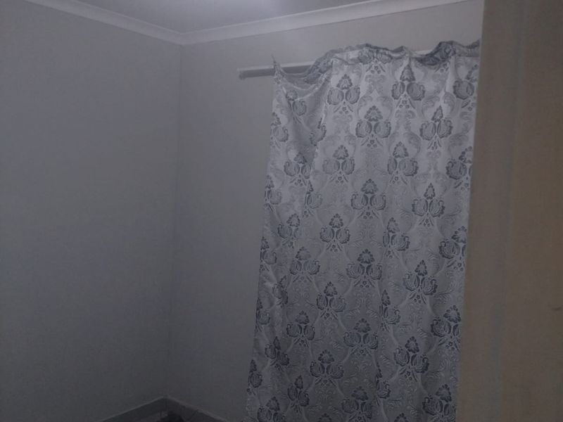 A simple, empty bedroom featuring tiled flooring and a ceiling light fixture, offering a blank canvas for personalization.