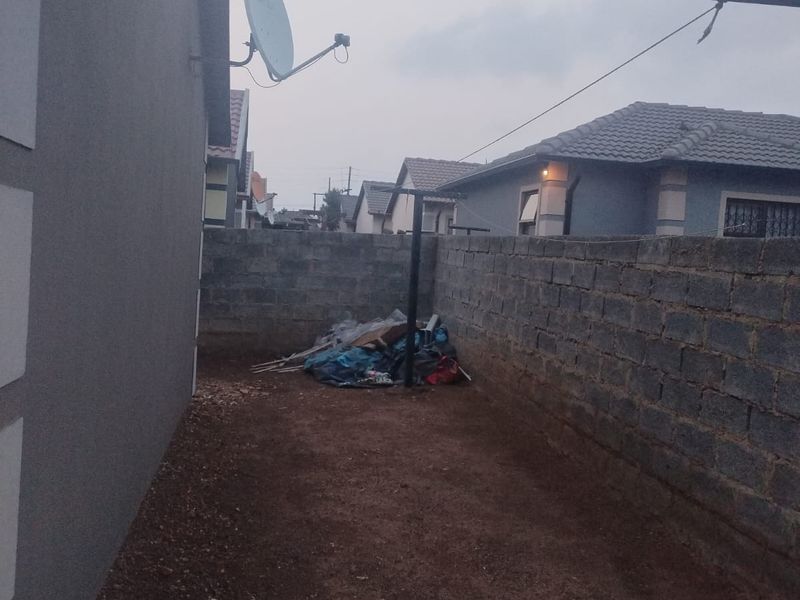 A side or rear yard area featuring a perimeter wall, satellite dish, and unpaved ground surface.