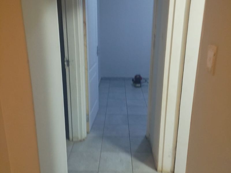 A narrow hallway featuring light-colored floor tiles and multiple internal doorways leading to adjacent rooms.