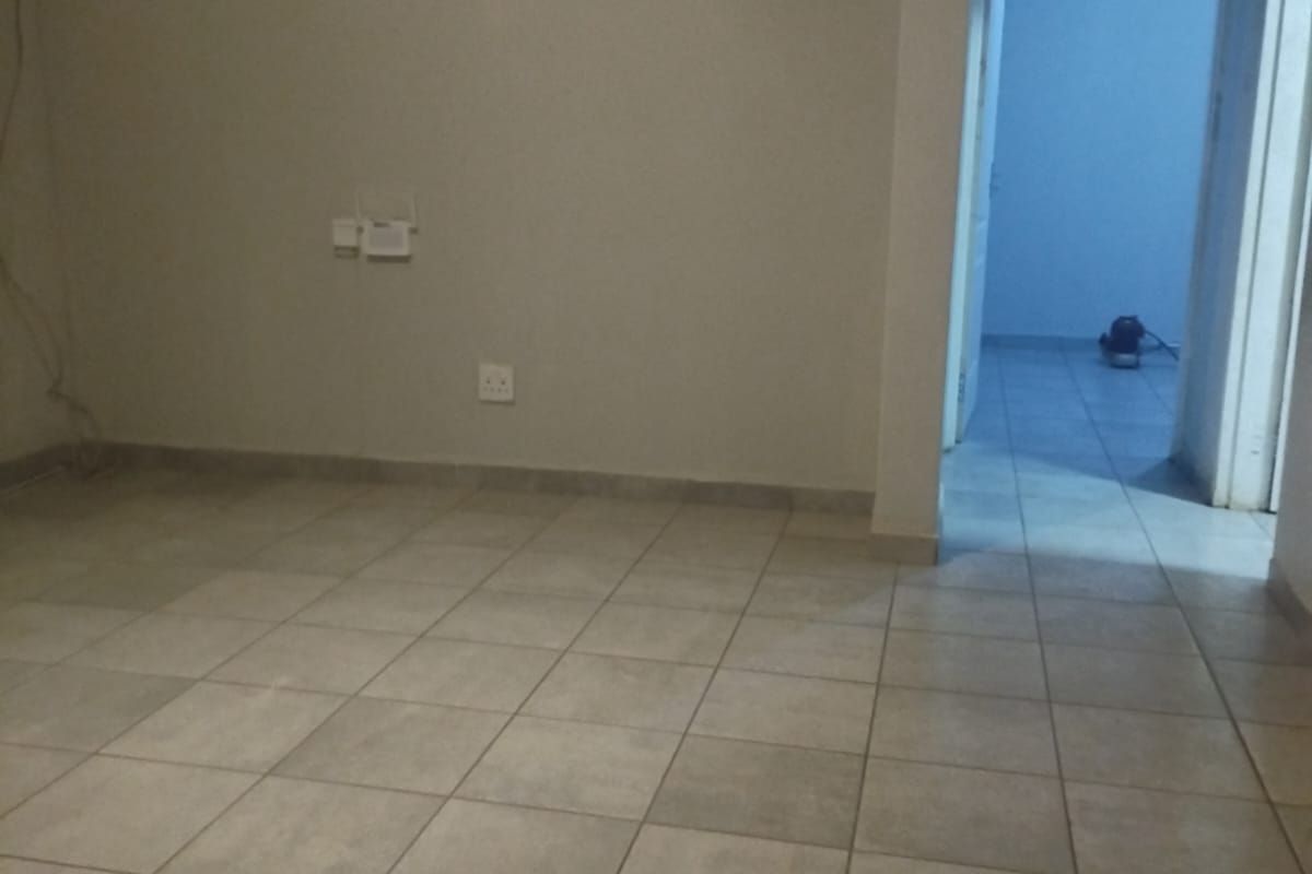 An empty living area featuring neutral ceramic floor tiles, clean walls, and a doorway leading to an adjacent room.