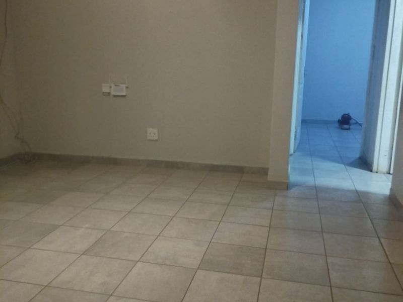An empty living area featuring neutral ceramic floor tiles, clean walls, and a doorway leading to an adjacent room.