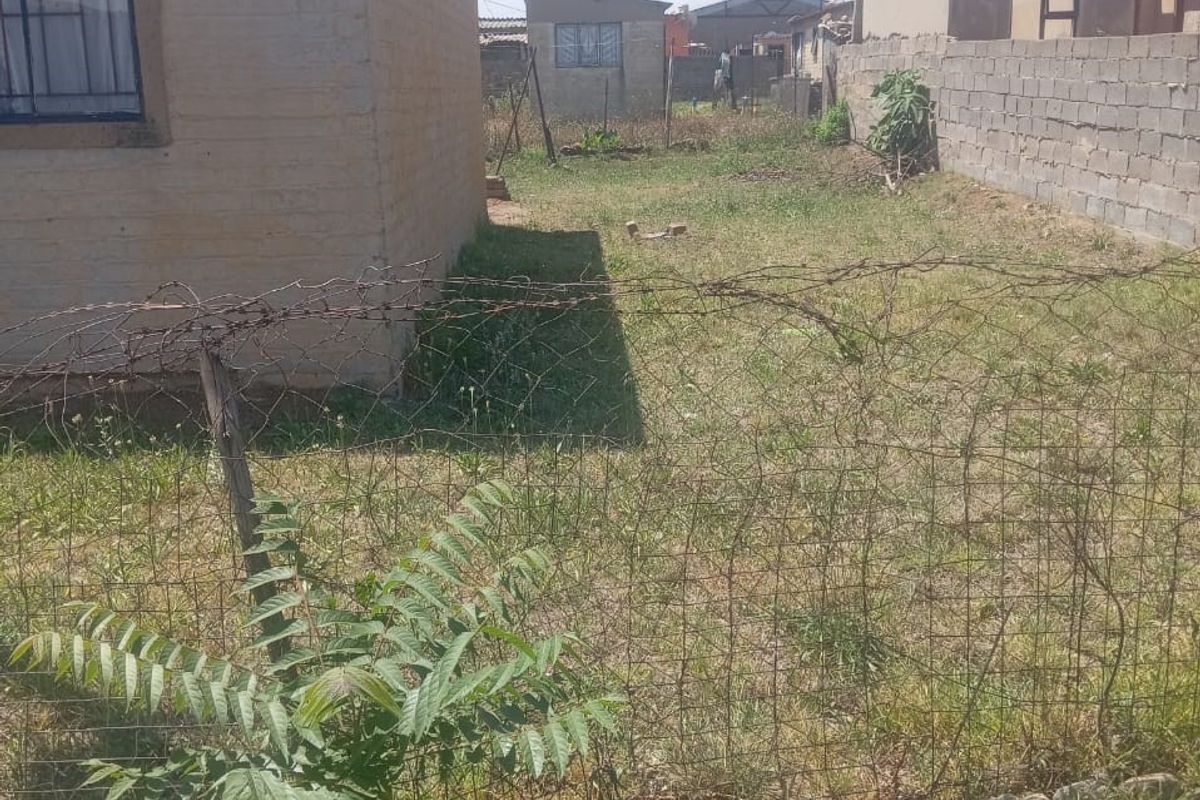 A view of the rear yard area featuring a perimeter wall, wire fencing, and an unpaved outdoor space.