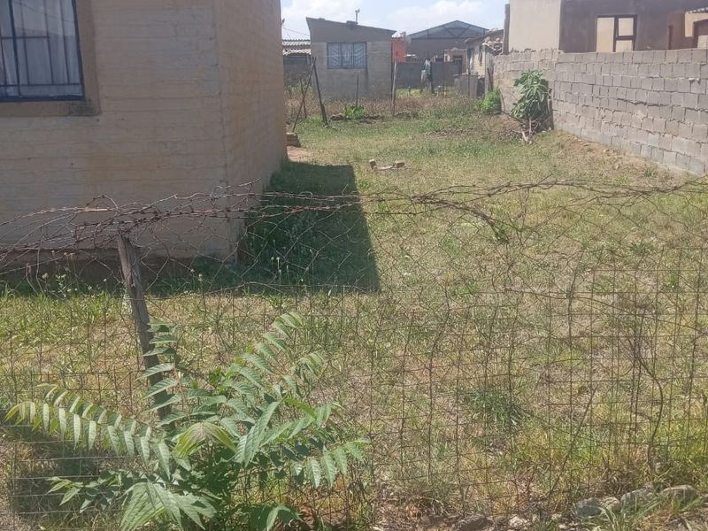 A view of the rear yard area featuring a perimeter wall, wire fencing, and an unpaved outdoor space.