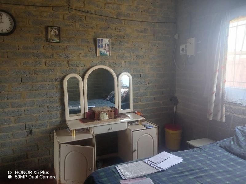 A bedroom featuring exposed brick walls and a window with security bars, requiring cosmetic updates to improve the overall finish and aesthetic appeal.