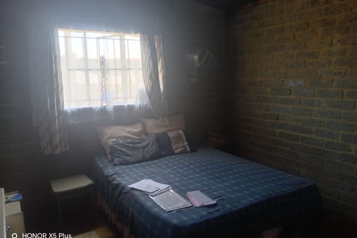 A bedroom featuring exposed brick walls and a window with security bars, requiring significant cosmetic updates to improve the finish and overall aesthetic.