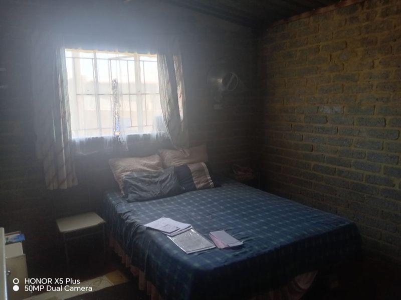A bedroom featuring exposed brick walls and a window with security bars, requiring significant cosmetic updates to improve the finish and overall aesthetic.
