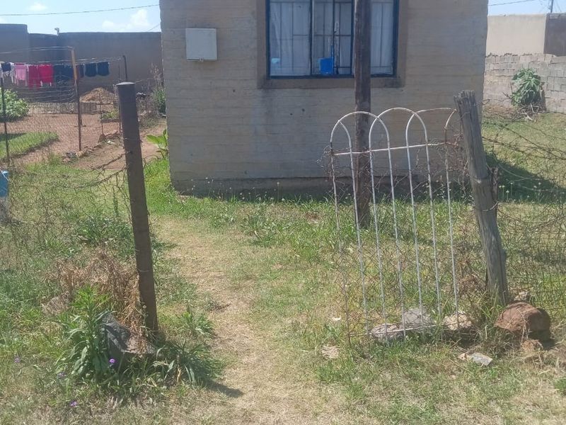 Rear view of a small residential structure featuring basic masonry construction, metal window frames with security bars, and an enclosed yard area.